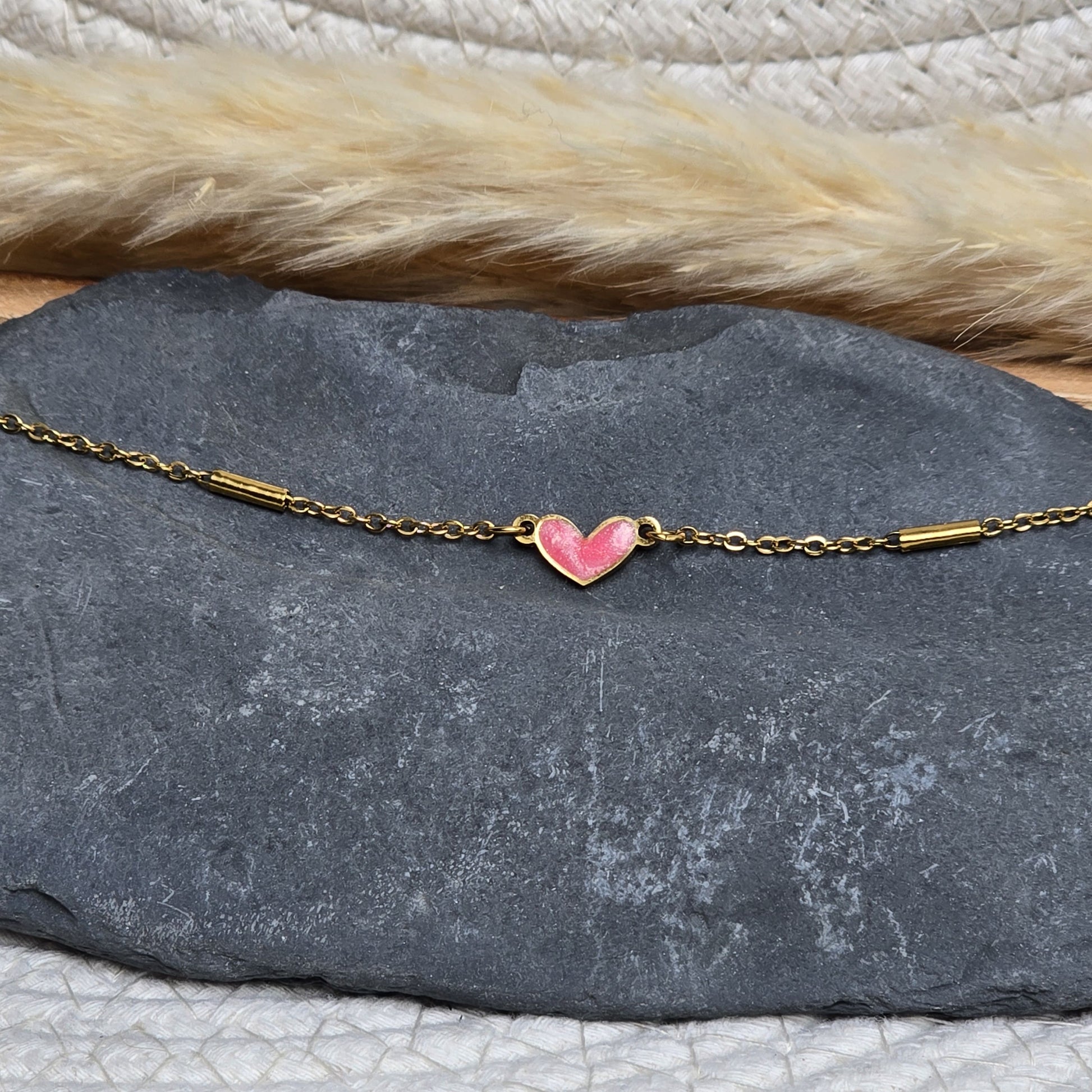 Bracelet doré porté au poignet avec cœur rose légèrement pailleté, création artisanale Zateka, 15 % reversés à LFS France