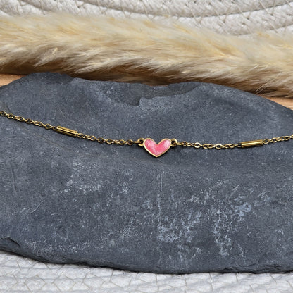 Bracelet doré porté au poignet avec cœur rose légèrement pailleté, création artisanale Zateka, 15 % reversés à LFS France