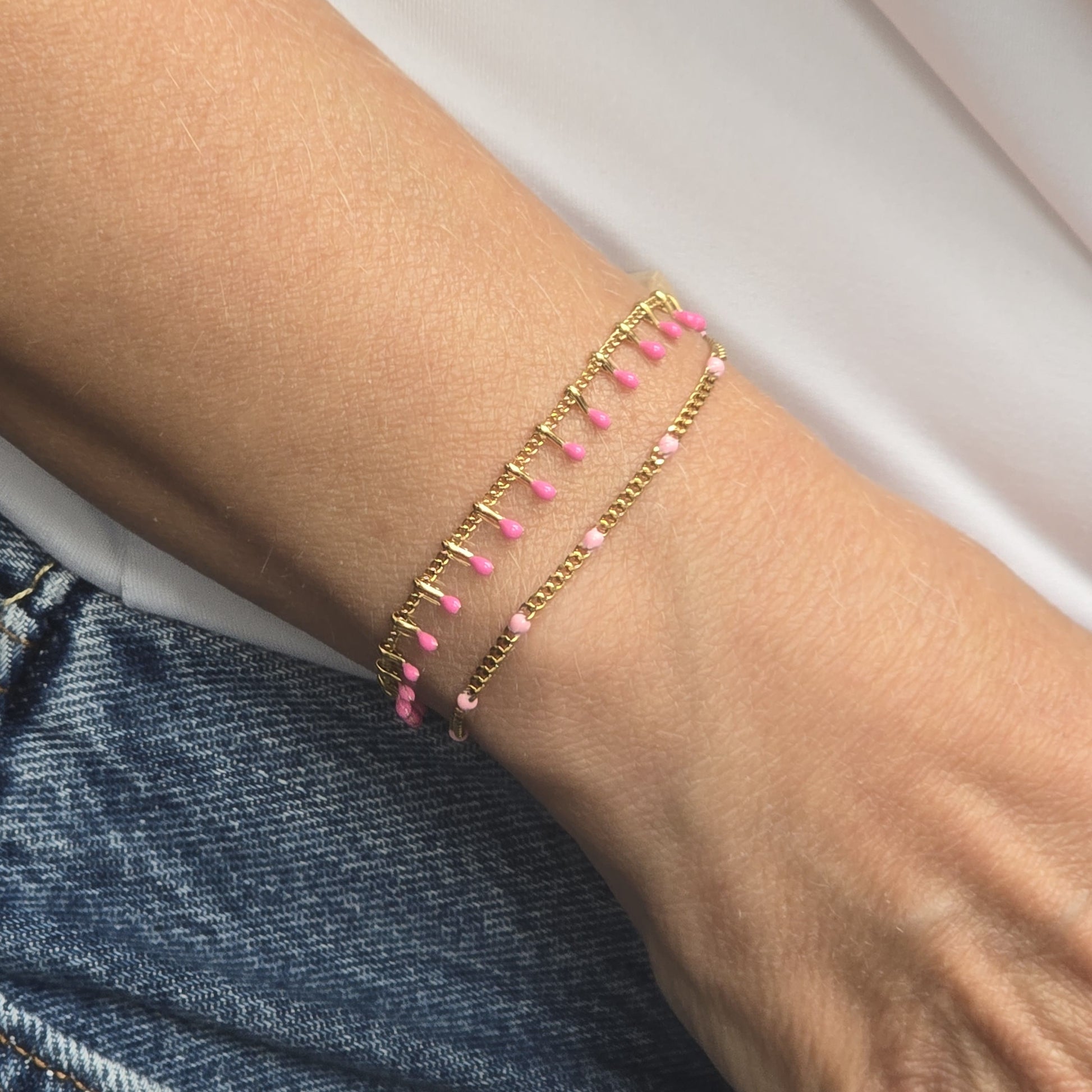 Bracelet doré porté au poignet, orné de petites billes émaillées rose poudré, bijou artisanal Zateka, 15 pourcents reversés à LFS France