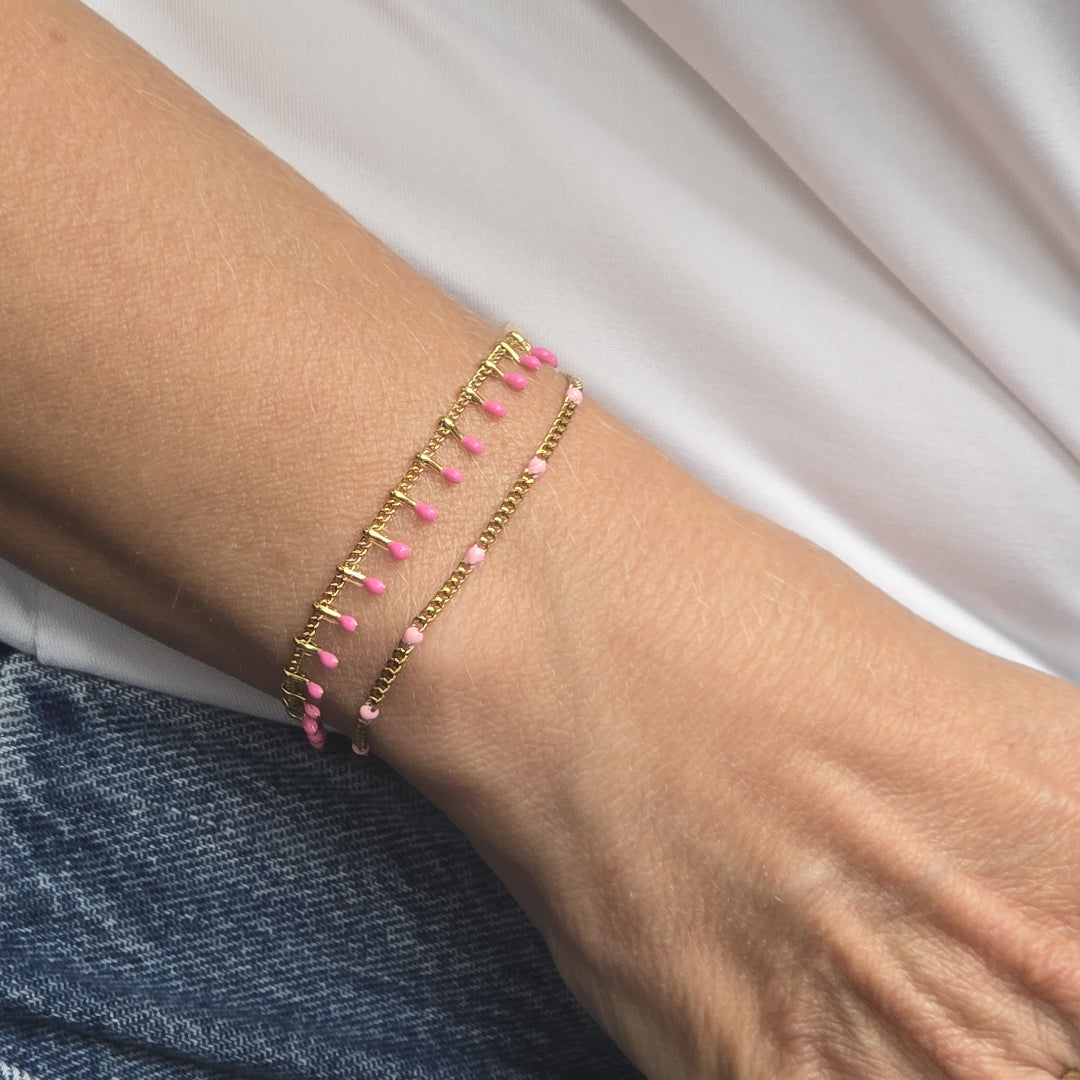 Bracelet fin doré porté au poignet, pampilles pendantes rose fuchsia, bijou solidaire Zateka