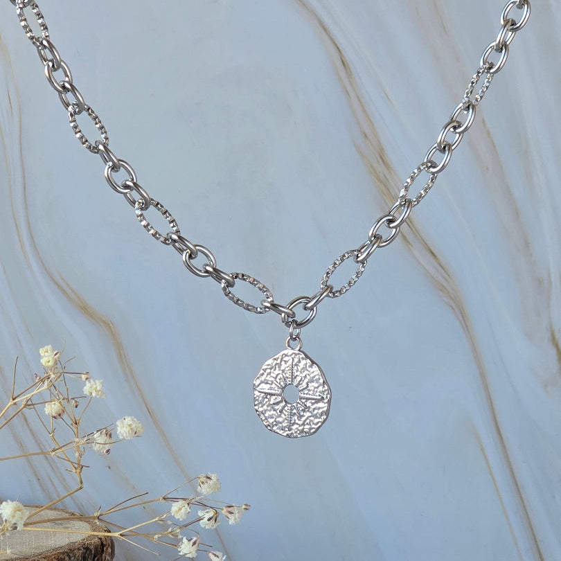 Détail du pendentif rond ajouré du collier LIBERTAS en acier inoxydable argenté